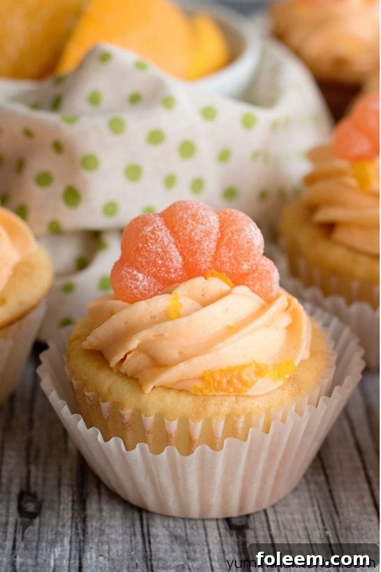 Several Orange Creamsicle Cupcakes with fluffy orange buttercream icing and small orange candies on top.