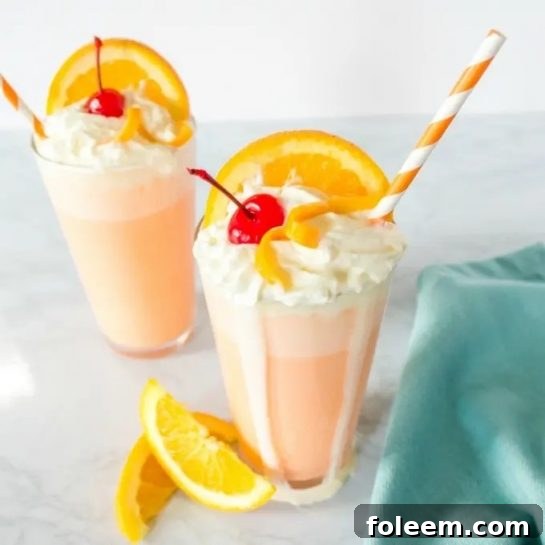 A tall glass of Orange Creamsicle Milkshake, garnished with whipped cream and an orange slice, evoking retro vibes.
