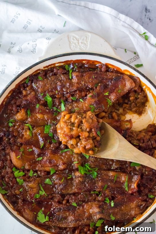 A vibrant platter of Beefy Baked Beans, featuring rich sauce, tender beans, seasoned ground beef, and crispy strips of peppered brown sugar bacon, perfectly garnished and ready to serve at a summer BBQ.