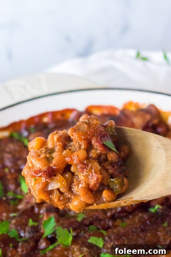 A close-up of a pot of Beefy Baked Beans, highlighting the rich, thick texture of the sauce and the visible pieces of ground beef, onions, and bell peppers, before the bacon topping is added.