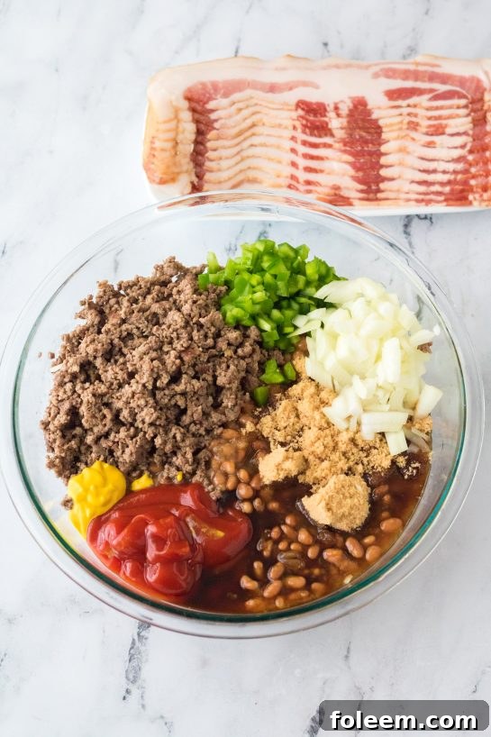 Hands mixing the various ingredients for the Beefy Baked Beans in a large mixing bowl, showing the uniform blend of beans, ground beef, vegetables, and the rich, dark sauce.