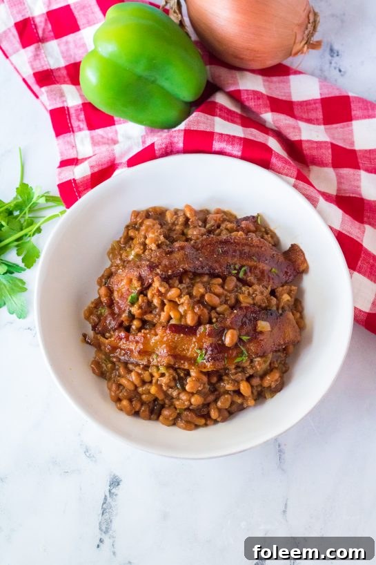 A large skillet filled with freshly baked Beefy Baked Beans, garnished with fresh parsley, showing the thick, bubbling sauce and crispy bacon pieces, ready to be served at a cookout or picnic.