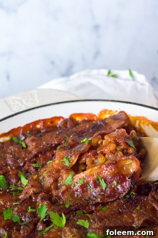 Close-up of a serving of Beefy Baked Beans in a rustic bowl, garnished with green onions, showcasing the rich texture and appealing presentation of the hearty side dish.