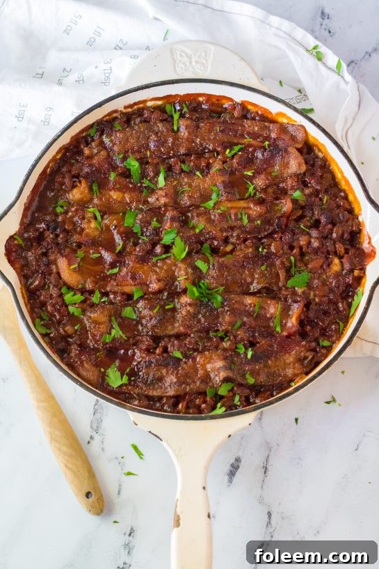A side view of a large baking dish filled with Beefy Baked Beans, generously topped with crispy bacon, cooked to perfection and ready to be enjoyed.