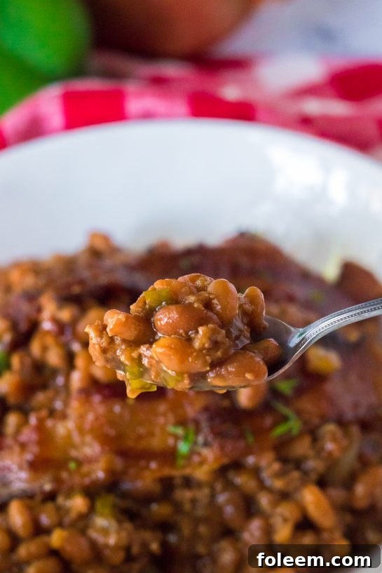 A large baking dish filled with Beefy Baked Beans, topped with crispy bacon and fresh parsley, presented as a centerpiece for a summer cookout.