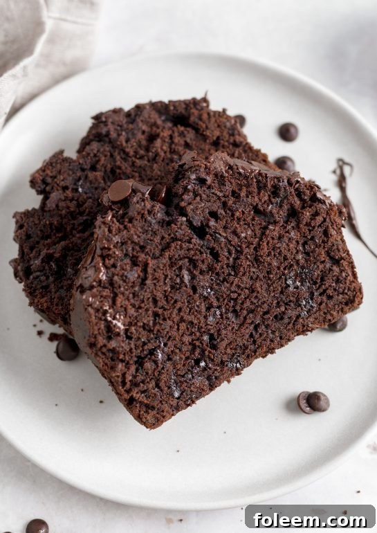 A generous slice of Chocolate Zucchini Bread on a plate, revealing its dense, moist crumb, luscious chocolate chips, and the delightful hint of green zucchini.