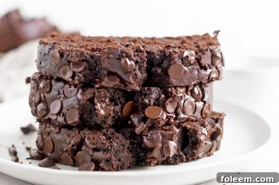 Close-up of a rustic wooden cutting board with slices of moist Chocolate Zucchini Bread, garnished with a few fresh zucchini slices, ready to be served.