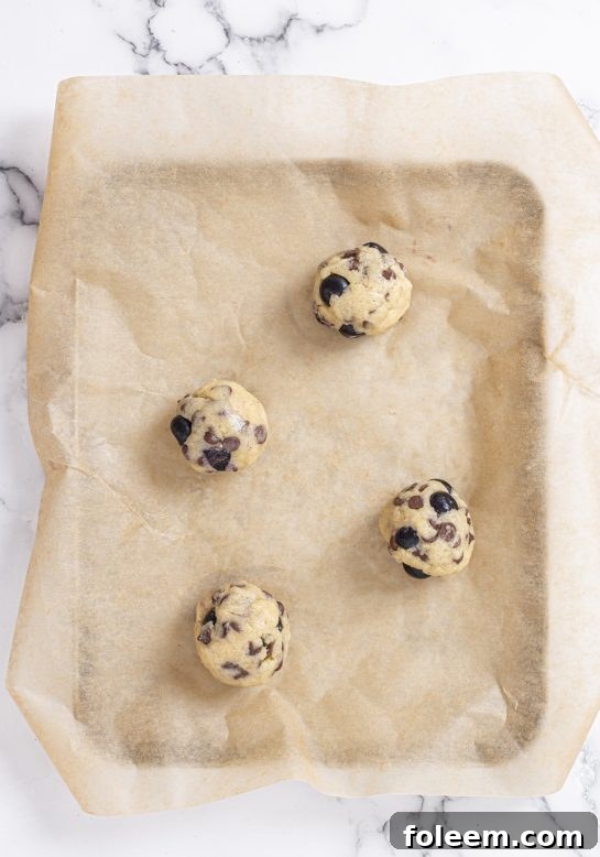 Freshly scooped Blueberry Chocolate Chip Cookie dough balls, topped with a luscious blueberry glaze, ready to go into the oven.