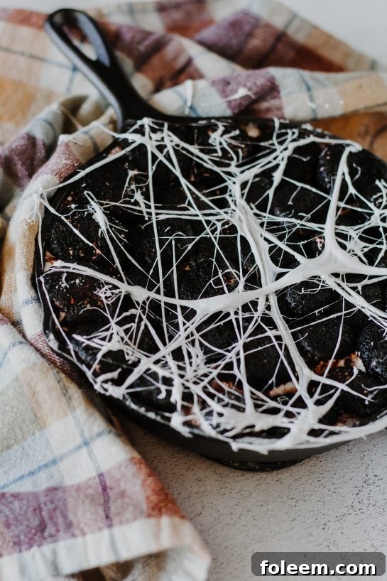 Close-up of the creepy Spiderweb S'mores Dip, showcasing the gooey white chocolate, browned marshmallows, and intricate marshmallow web, ready to be enjoyed with dippers