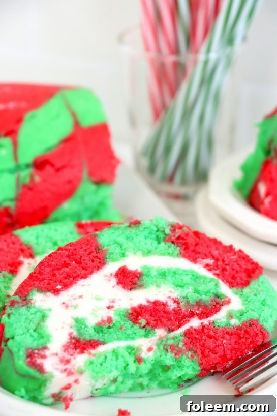 A beautifully sliced Christmas Cake Roll showcasing its vibrant red and green spiral pattern and creamy white frosting, ready to be enjoyed.