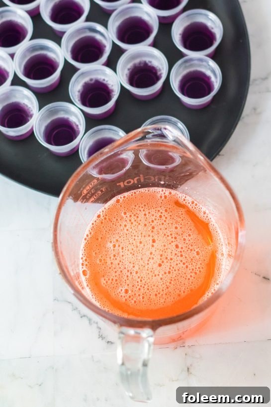 Carefully pouring the vibrant orange Jell-O layer, a key step in creating the colorful Halloween jello shots recipe.