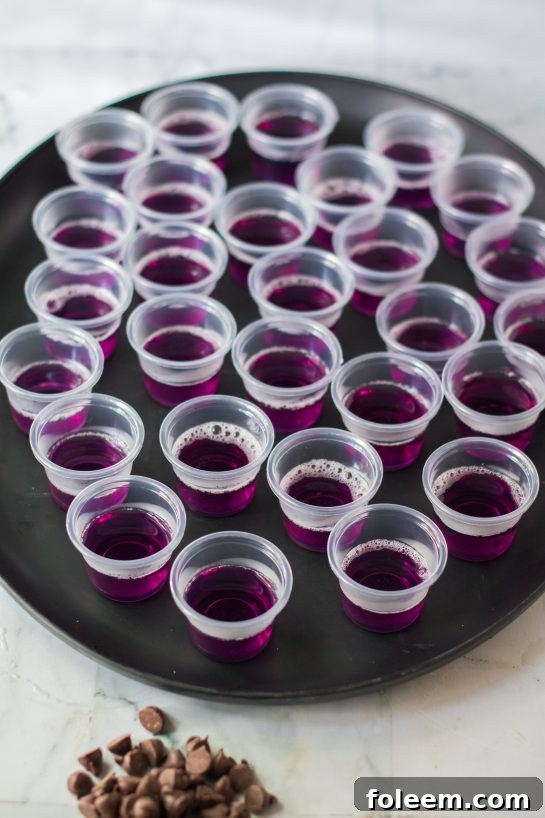 The process of making Halloween Jello Shots, showing the purple layer being poured into individual plastic cups.