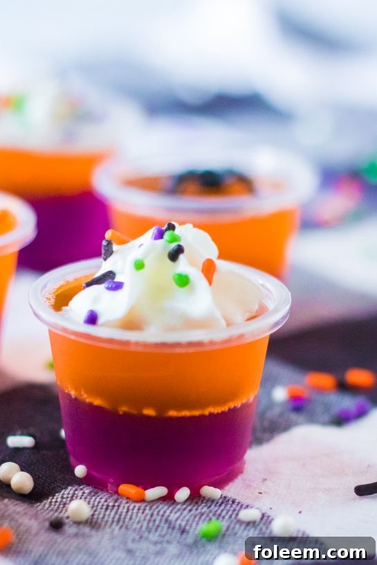 Close-up of finished Halloween Jello Shots garnished with whipped cream and festive sprinkles, perfect for a Halloween party.