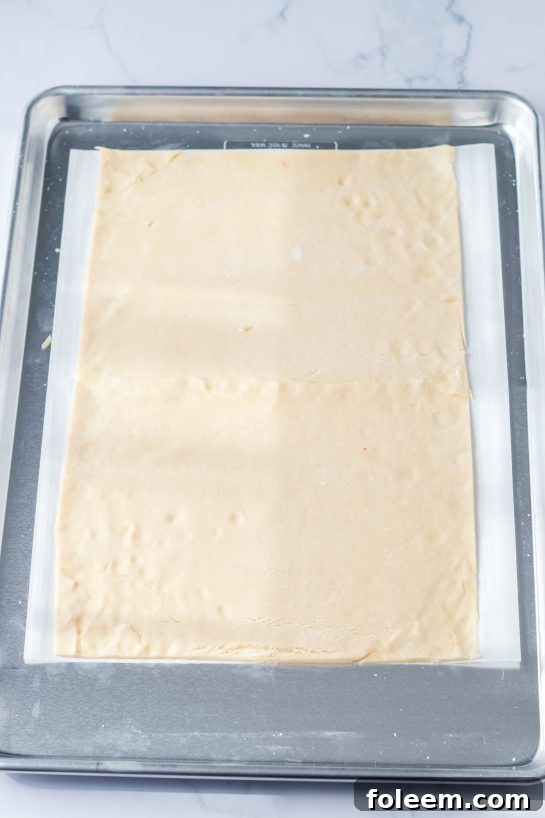 Spreading out the ready-to-bake pie dough on a parchment-lined sheet pan, preparing the base for the pop-tarts.