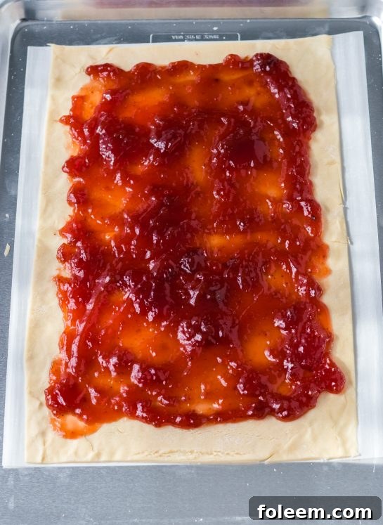 Carefully spreading a generous layer of strawberry jam onto the rolled-out pie crust, leaving a border for sealing.