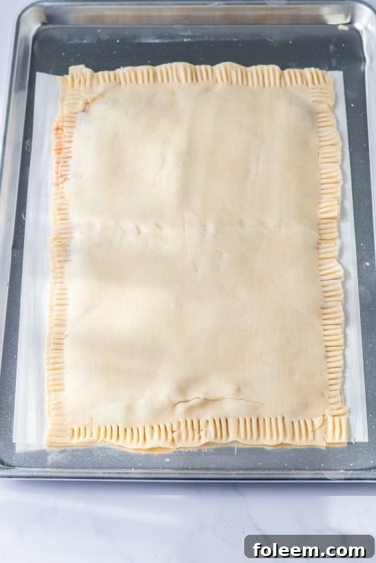 Sealing the edges of the Sheet Pan Strawberry Poptarts with a fork, creating a classic crimped pattern.