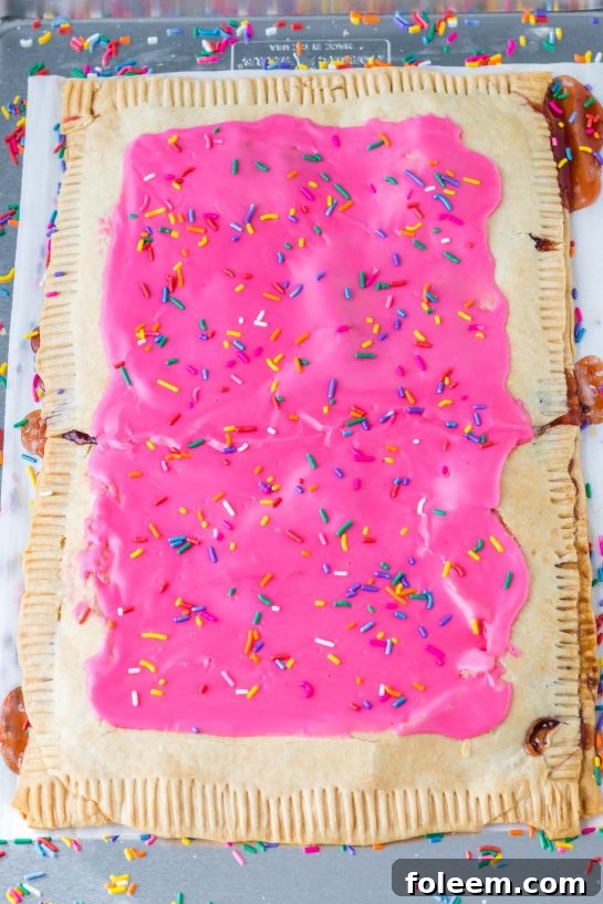 Generously spreading the homemade pink strawberry icing over the cooled Sheet Pan Strawberry Poptart, creating a smooth, even layer.