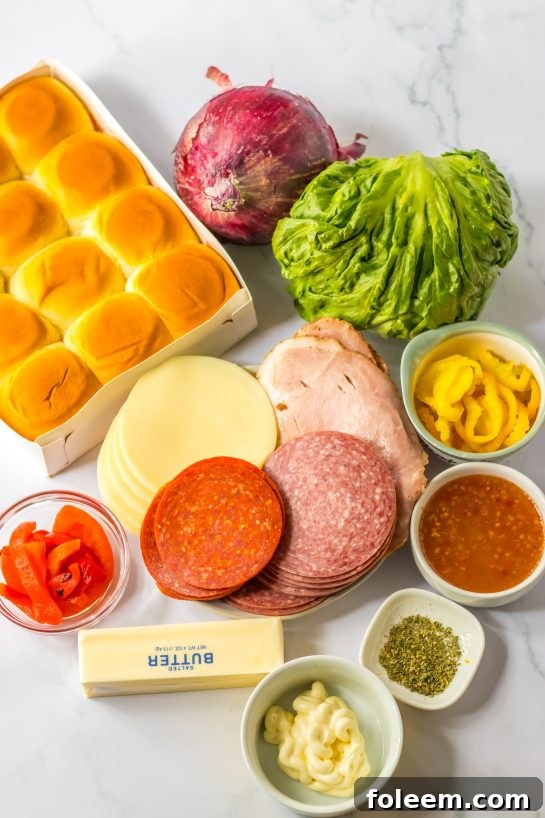 Ingredients for Italian Sub Sliders laid out on a table, including deli meats, cheese, rolls, and vegetables.