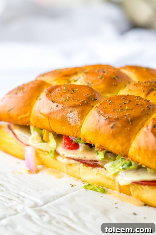 Freshly baked Italian Sub Sliders, golden brown and cheesy, ready to be sliced and topped.