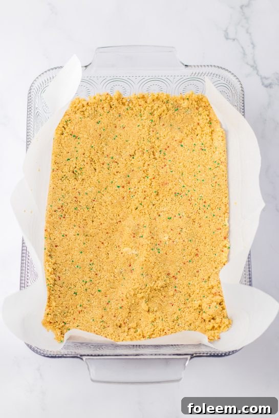 Pressing a festive vanilla cookie crust into a 9x13 pan, forming the base for the Christmas Cookie Lush.