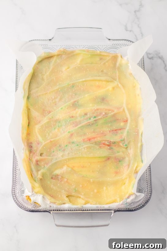 Spreading a creamy pudding layer evenly into the pan, a key step in assembling the Christmas Cookie Lush dessert.