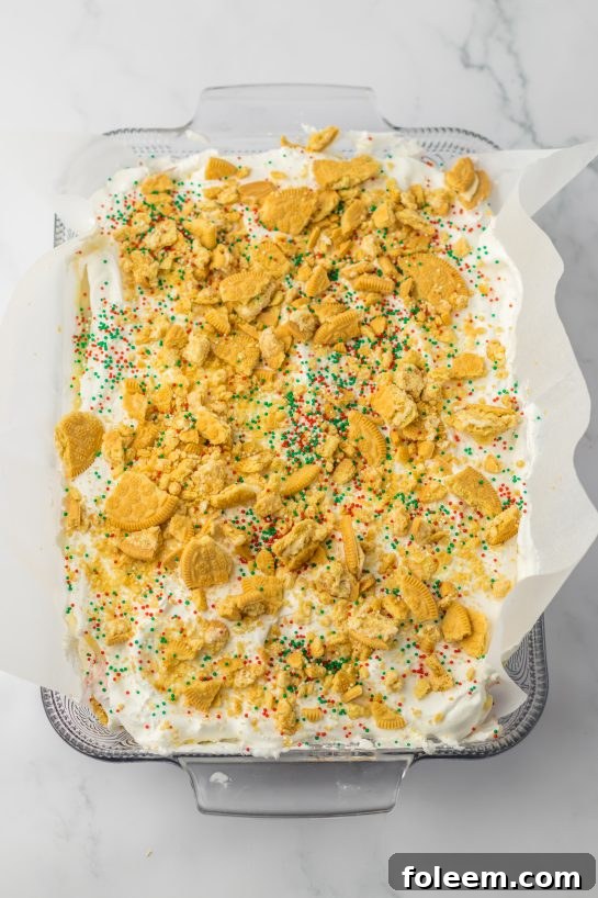 Sprinkling crushed Oreo cookies and festive sprinkles over the whipped topping, the final delicious touches for Christmas Cookie Lush.