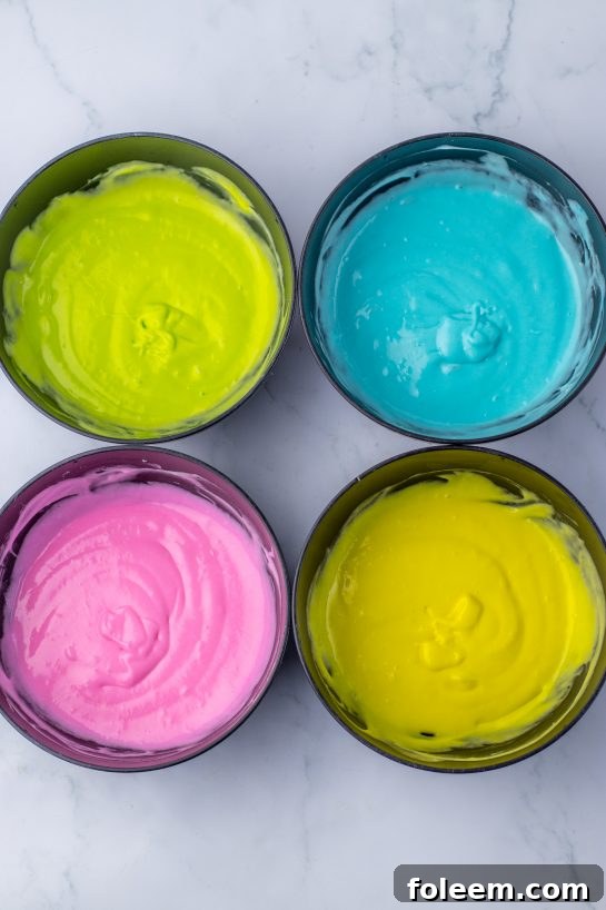 Dividing cake batter into bowls and adding pink, green, blue, and yellow food coloring for the vibrant Easter Poke Cake.