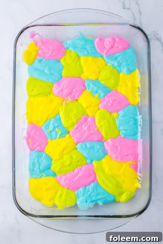Carefully pouring dollops of vibrantly colored cake batter into a baking dish before baking the Easter Poke Cake.