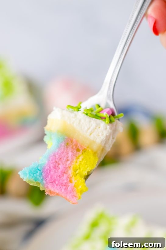 A close-up of a fork holding a delicious bite of Easter Poke Cake, showing the distinct colored layers, pudding, and whipped cream.