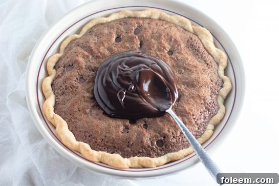 Smooth homemade chocolate ganache being spread over the cooled Cosmic Brownie Pie, creating a beautiful finish.