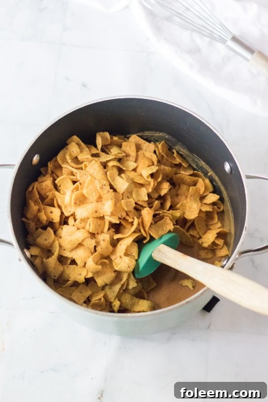 Frito corn chips being gently mixed with the creamy peanut butter caramel in a large pot