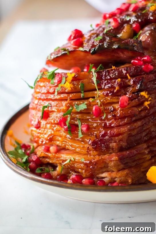 A perfectly glazed Christmas ham, garnished with orange zest, pomegranate seeds, and fresh parsley, ready for holiday celebration.