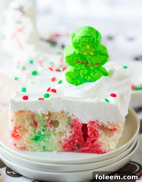 Vibrant Christmas Poke Cake, featuring white cake with green and red Jell-O, topped with whipped cream, holiday sprinkles, and marshmallows, ready to be a delightful festive dessert.