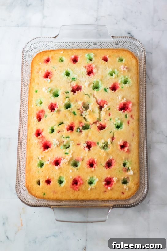 Red and green Jell-O mixtures being poured into the poked holes of the Christmas Poke Cake, alternating colors.