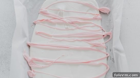 The artistic process of drizzling melted pink chocolate over a bed of white chocolate for the Circus Cookie Bark recipe.