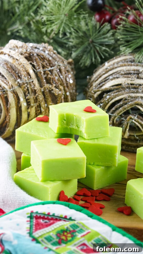 Photo of the finished Grinch Fudge recipe with the heart sprinkles with a bite taken out of one piece of the fudge.