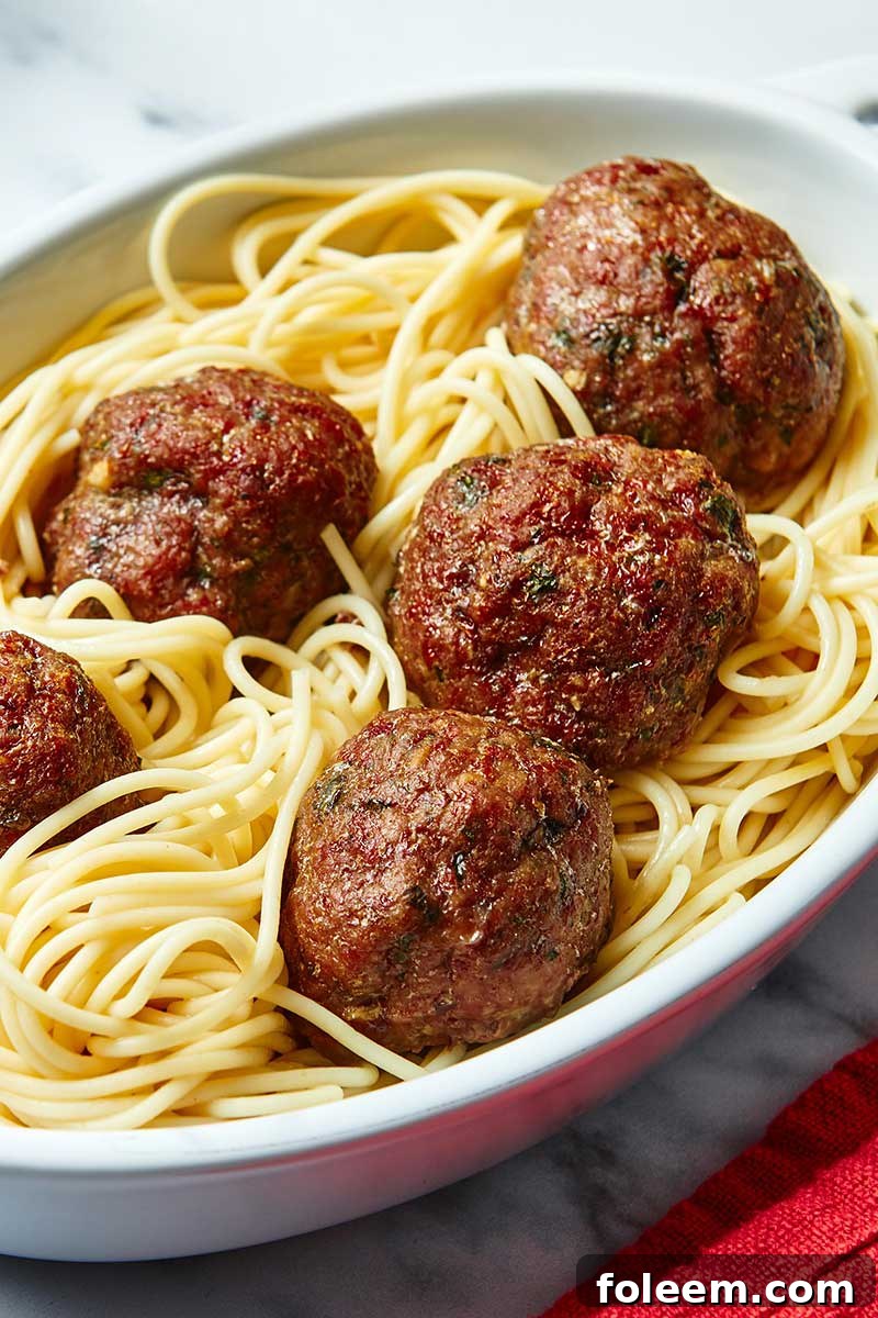 Giant meatballs on spaghetti in white platter.
