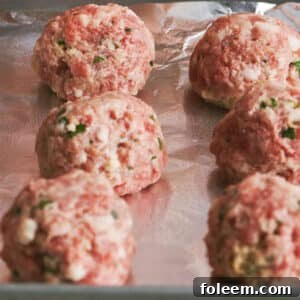 Uncooked meatballs on foil-lined baking sheet.