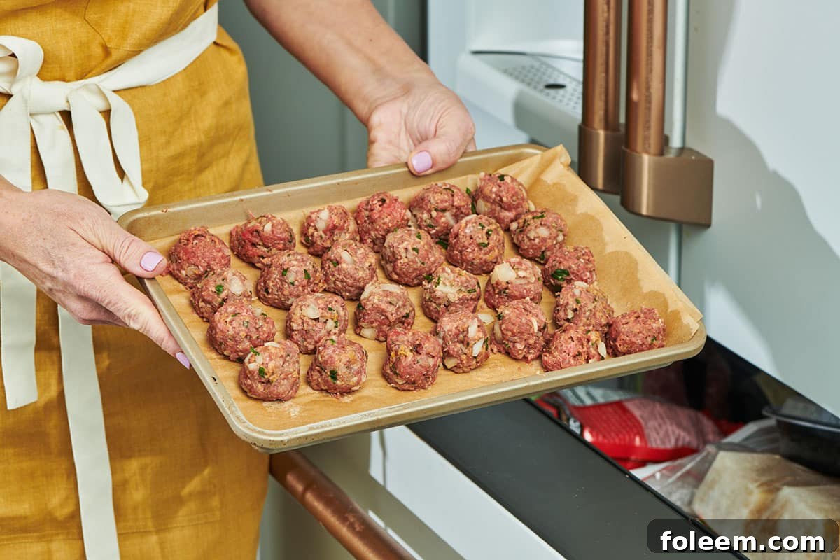 Woman placing tray of meatballs in freezer.