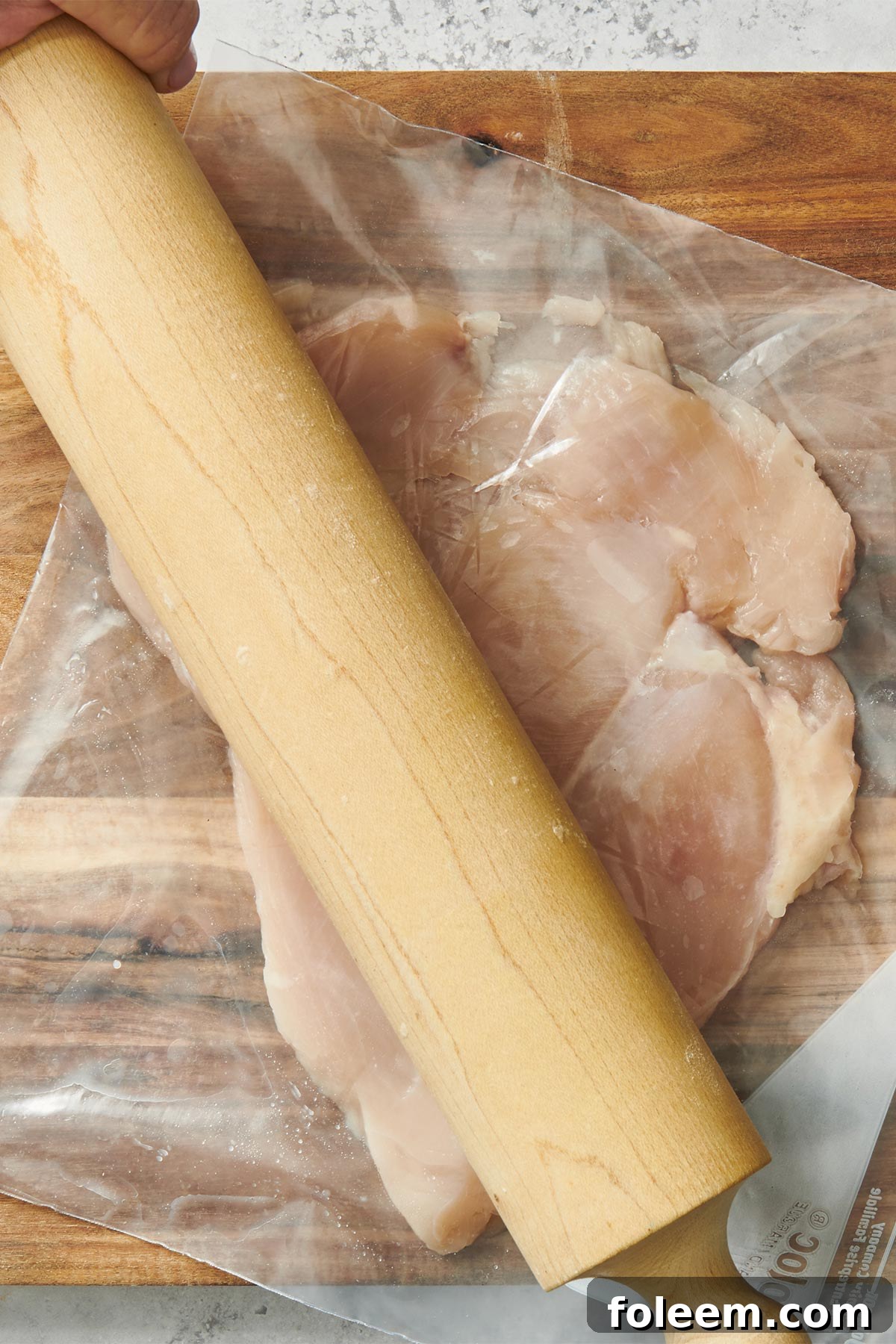 Pounding chicken flat with rolling pin.