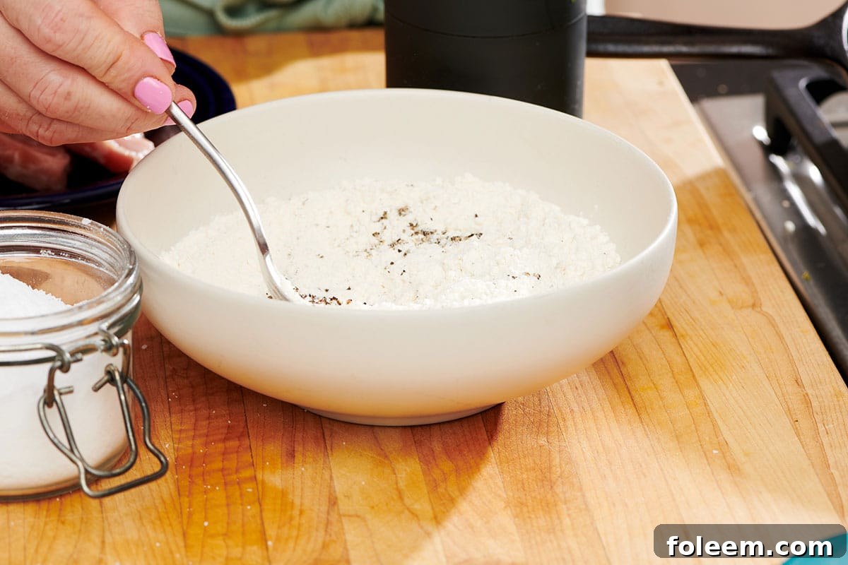 Mixing herbs and spices into flour in bowl.
