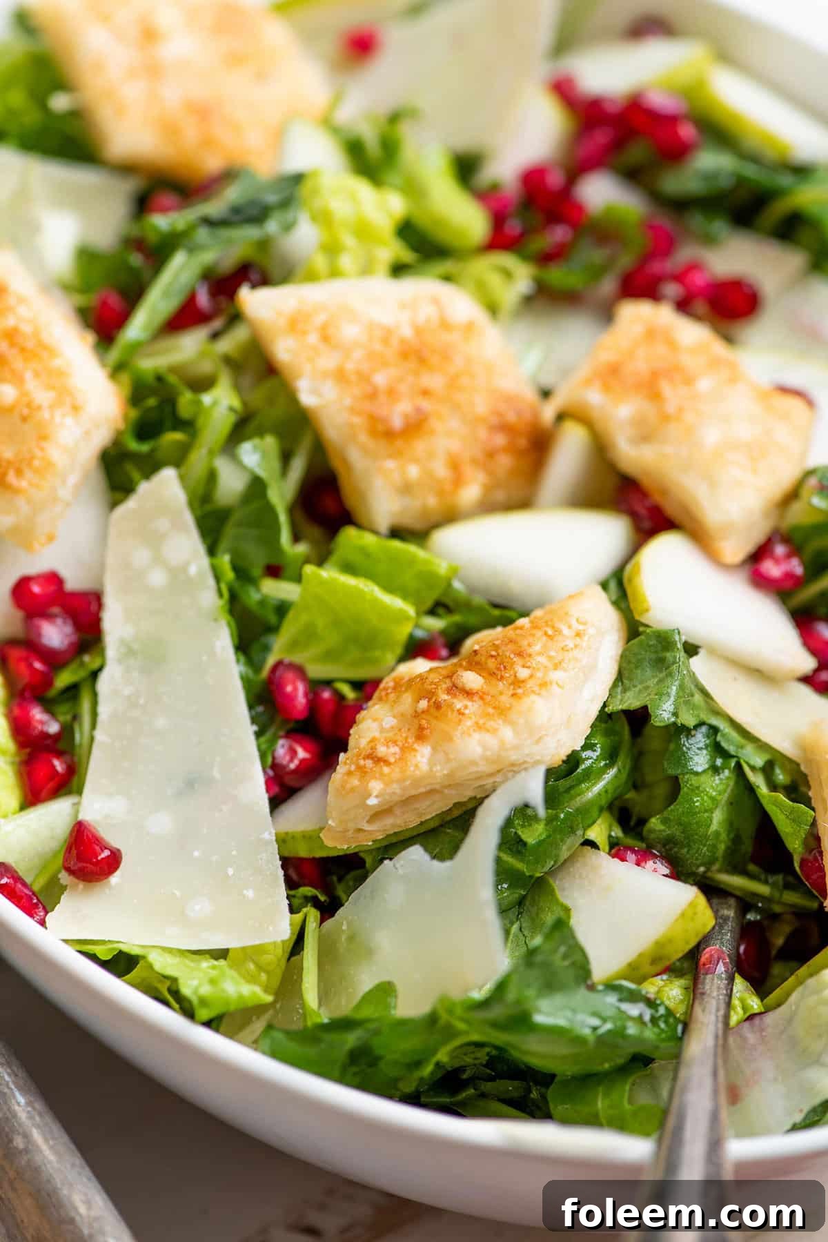 Salad in bowl with puff pastry croutons, pears, and pomegranate.
