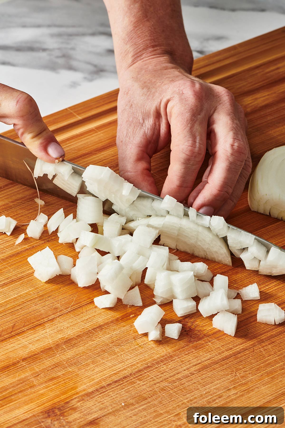Woman dicing white onion with knife on cutting board.