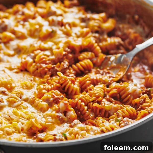 Spoon in pan of beef enchilada casserole with pasta.