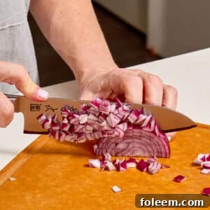 Woman dicing red onion on cutting board with knife.