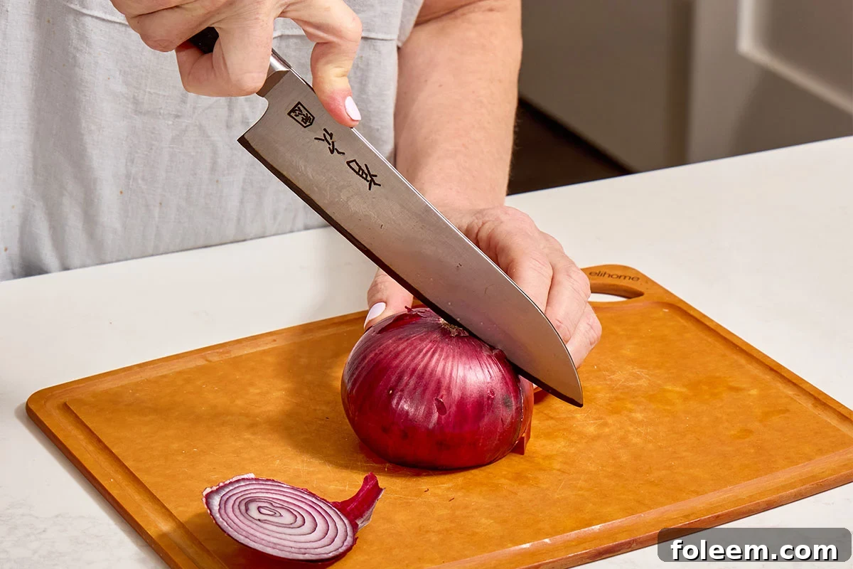 Cutting white onion in half with knife.