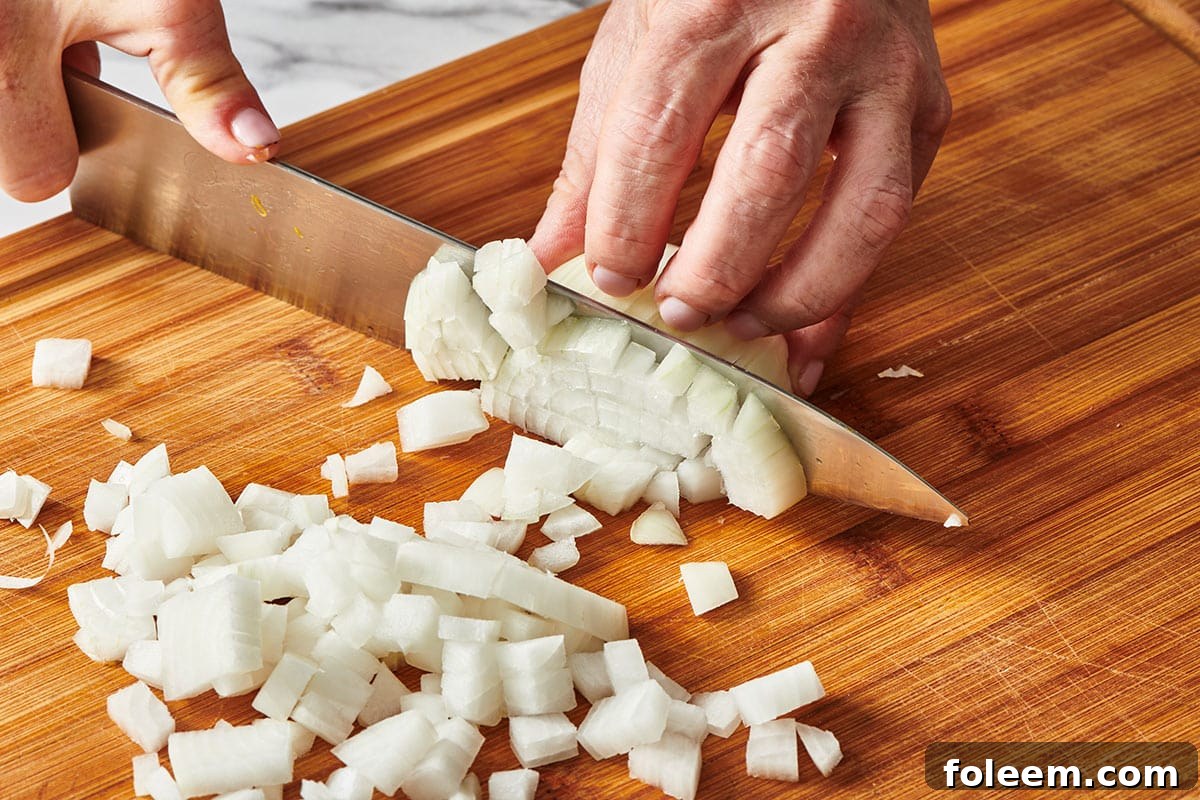 Woman dicing white onion on cutting board.