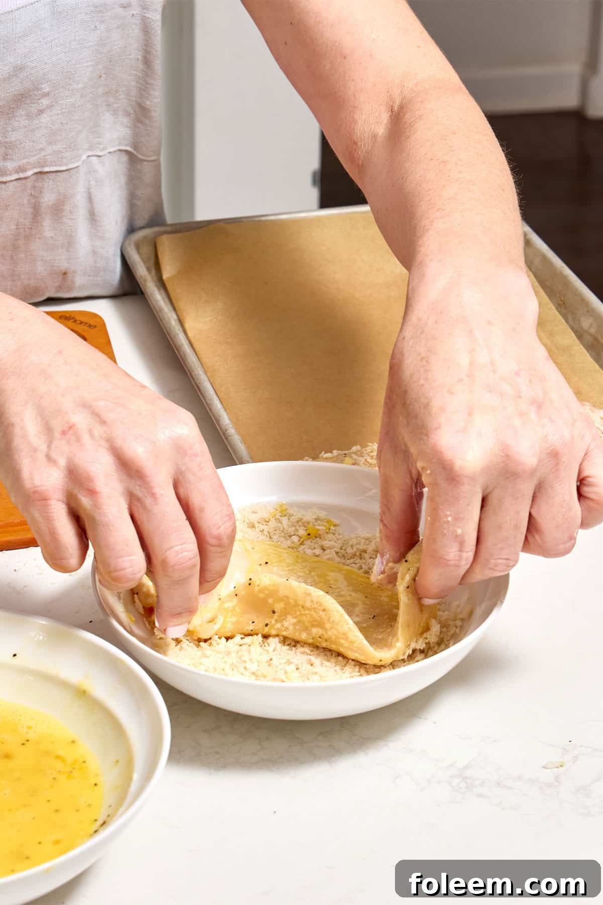 Woman dredging egg-coated chicken cutlet in panko breadcrumbs.