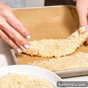 Woman placing breaded chicken cutlet on parchment-lined baking sheet.