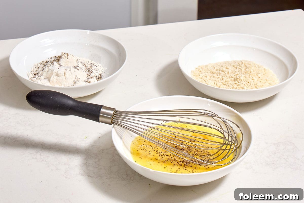 Seasoned flour, beaten eggs, and breadcrumbs in shallow white bowls on counter.
